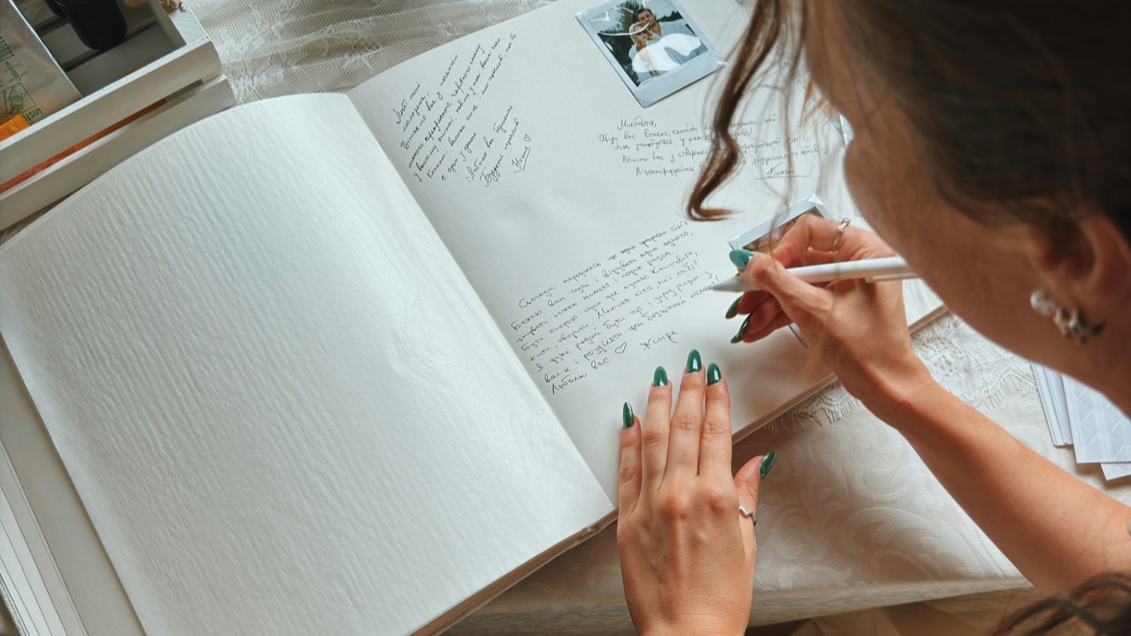 Gościni wpisuje się do papierowej księgi gości, obok leżą zdjęcia z polaroidu