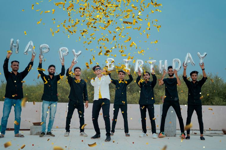 Grupa osób skacząca pod napisem Happy Birthday w konfetti